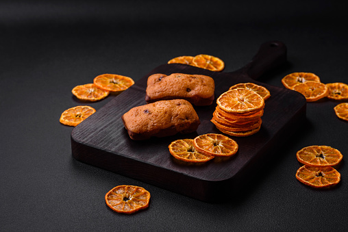Delicious chocolate muffins and dried round shaped slices of bright orange color tangerine on a dark textural background