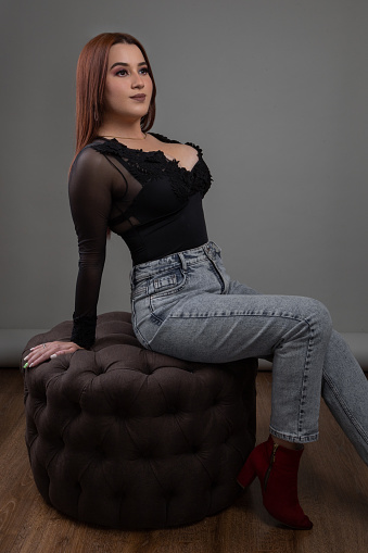 posing sitting on a pouffe a latin woman with makeup and wearing a bodysuit and jeans, studio portrait of a young person, relaxed