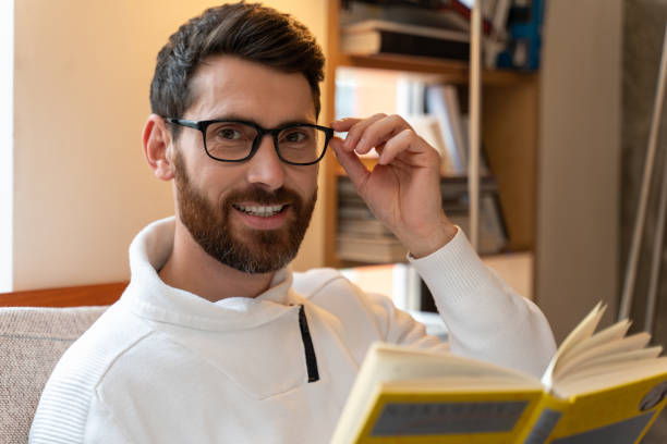 istock Bearded man wearing glasses reading interesting book with happy expression 1472364037