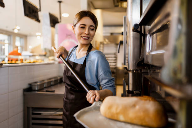 istock Female baker in uniform working in bakery production baking pastry in the oven 1472371006