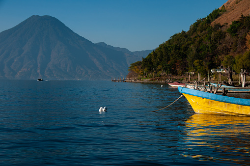 A yellow and blue boat on the shore of Lake Atitlan with a volcano in the background