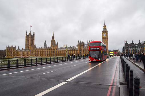 London, UK -  January 3 2023: A  red double decker bus passes by the Houses of Parliament and Big Ben on Westminster Bridge