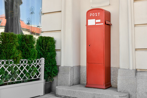 Red postbox near beige building on summer day