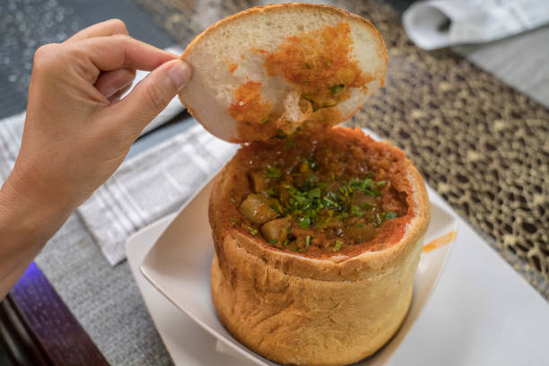 Portion of a soup in a bread bowl on the table and female hand.