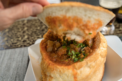 Portion of a soup in a bread bowl on the table and female hand.