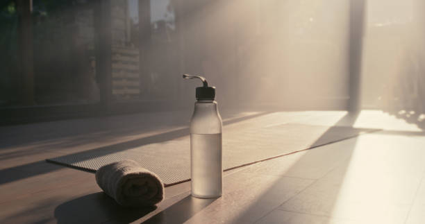 Water bottle, towel and exercise mat in wellness studio or gym floor for yoga, fitness and training. Healthy lifestyle, diet and mockup space with lens flare for advertising health club subscription botella de agua, toalla y colchoneta de ejercicios en el estudio de bienestar o en el gimnasio para yoga, fitness y entrenamiento. estilo de vida saludable, dieta y espacio de maqueta con destello de lente para la suscripción al club de salud publicitario