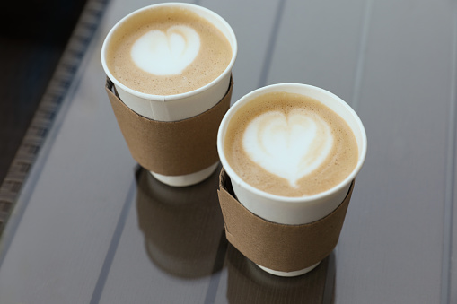 Paper takeaway cups of coffee with cardboard sleeves on glass table, above view