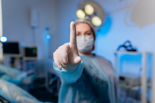 Proctóloga vestida con uniforme médico posa mostrando dedos y sonriendo en el hospital antes de la operación photo