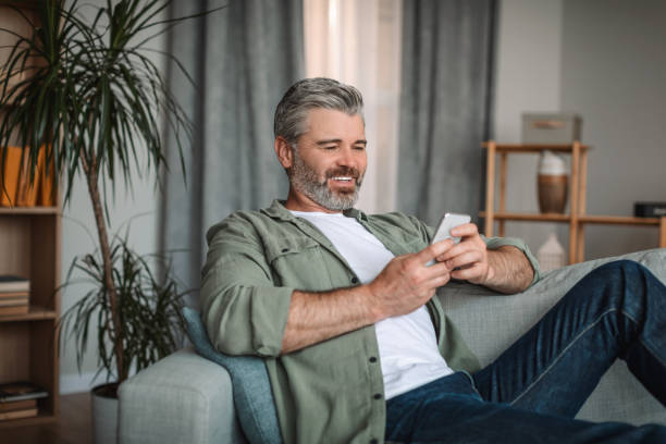 istock Smiling caucasian mature man with beard watching video, playing game on smartphone 1472383538