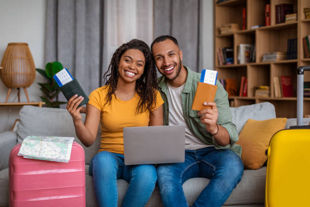istock Loving black spouses planning trip, using laptop and booking hotel, having tickets, sitting with packed clothes 1472383595