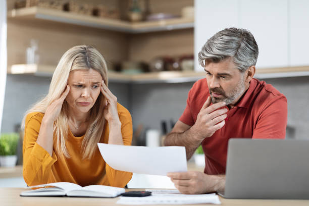 istock Stressed husband and wife sitting at kitchen table, reading documents 1472384626