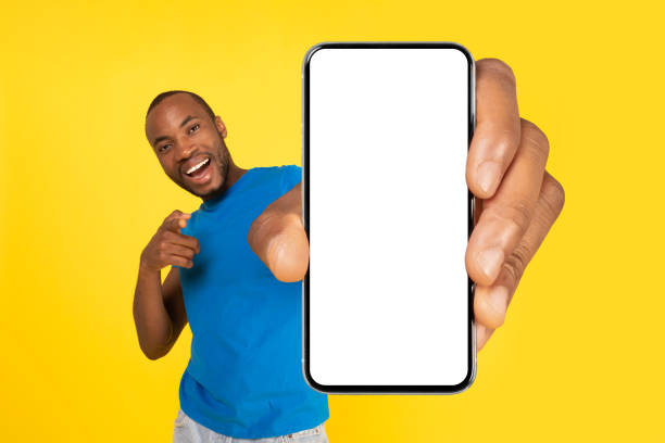 istock Joyful Black Guy Holding Phone With Large Screen, Yellow Background 1472384882
