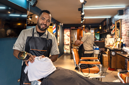 Portrait of an African American barber at work smiling and looking at the camera while massaging a client's face in the barber shop.