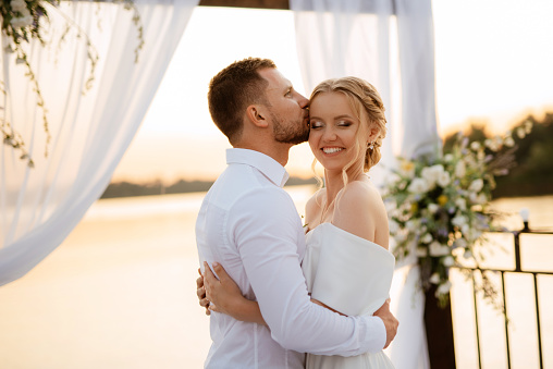 bride and groom against the backdrop of a yellow sunset on a pier near the river