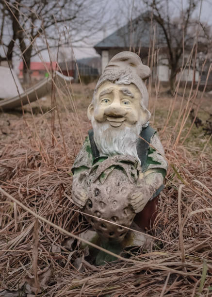 istock Old garden gnome figure with peeling paint among dry grass 1472398026