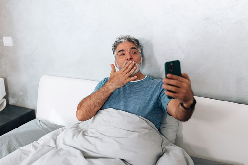 This mature man likes to stay on top of things, even before he gets up from bed, as he checks his phone to catch up on the latest news and messages