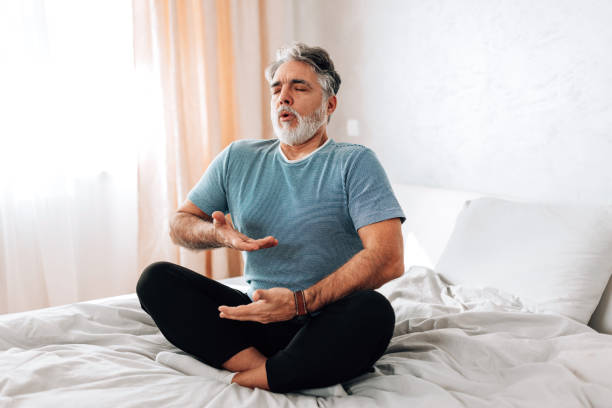 Yoga in Bed. This Man Shows How to Create a Peaceful Morning Routine Watch as this man demonstrates his peaceful morning routine, practicing yoga in bed. He moves his body with ease and grace, promoting relaxation and calmness deep stock pictures, royalty-free photos & images