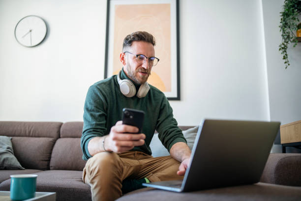 istock Man sitting on sofa and using laptop at home. 1472405421