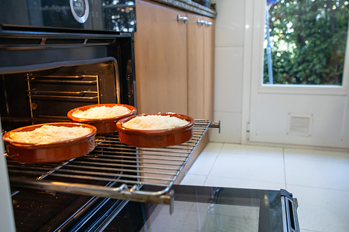 Ceramic pans with casserole placed on grating in opened oven during lunch preparation in kitchen at home
