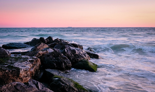 Soft pink sunset falls at the horizon with waves crashing on the jetty.