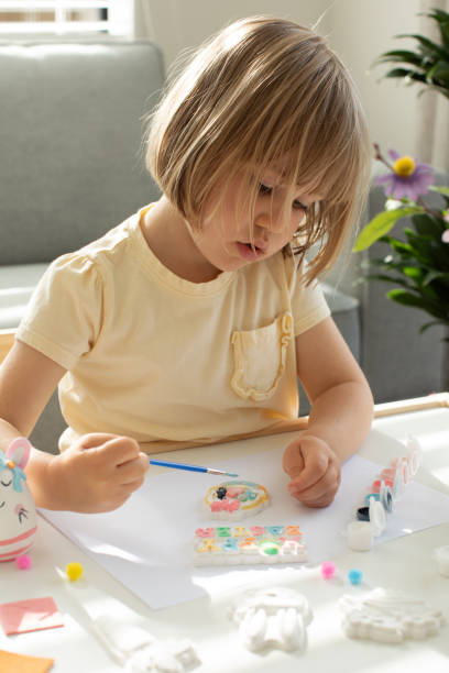 istock A cute little girl is sitting at a table and doing Easter crafts, coloring Easter figurines. Creativity and hobbies. 1472415152