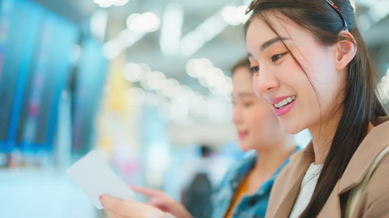 Asian young woman passenger checking depature boarding pass in airport. Attractive beautiful female tourist friends feeling happy and excited to go travel abroad by airplane for holiday vacation trip.