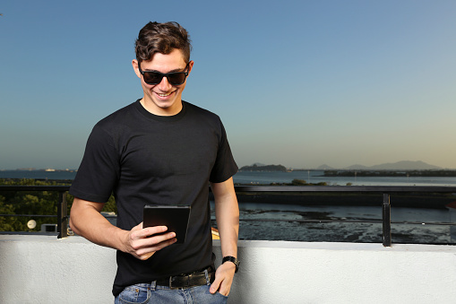 Young man looking at his tablet while enjoying the summer outdoors as the sunset goes down. Lifestyle. Man in black outdoor sweater with space for text.