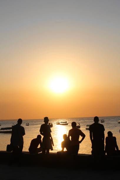 istock Young men watch the sun set from the beach 1472428480