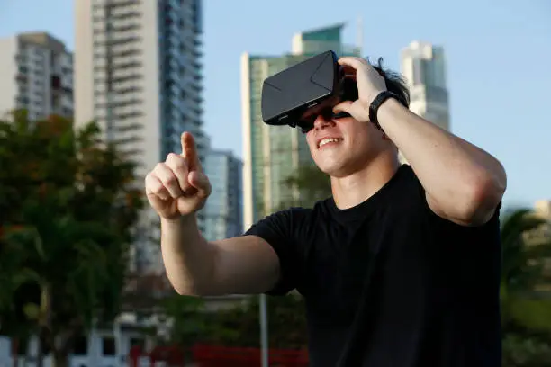 Chico joven con gafas de realidad virtual al aire libre con ciudad de fondo y sueter negro