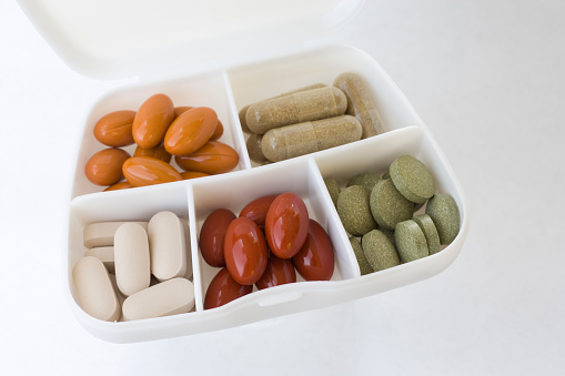 Nutritional supplements in a plastic travel container.  Top left, orange capsules - Coenzyme Q10 & resveratrol