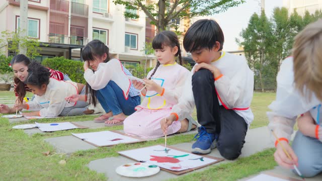Group of student coloring on painting board outdoors in school garden. Adorable children learn how to draw art picture with watercolor paint and brush enjoy creative fun activity at elementary school.