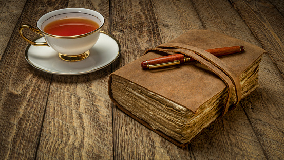 antique leather-bound journal with a cup of tea and pen on a rustic wooden table