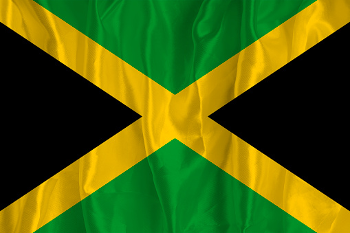 The flag of Jamaica on a silk background is a great national symbol. Texture of fabrics The official state symbol of the country.