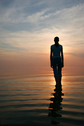 Silhouette of young woman standing in a water at the sunset