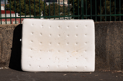 Discarded old mattress on a footpath against a wall.
