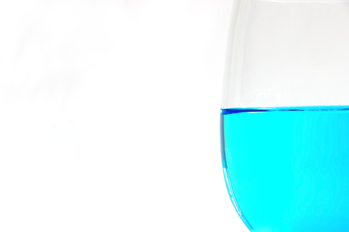 Closeup of a glass half filled with blue drink isolated against plain, white background. Copy space.