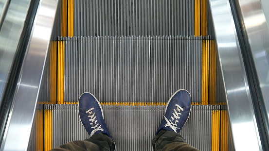The shoes of a young man going down an escalator stairs