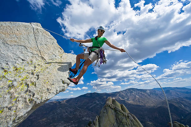 Climber rappelling from the summit of a rock spire in The Sierra Nevada Mountains, California, on a cloud filled sky, summer day.