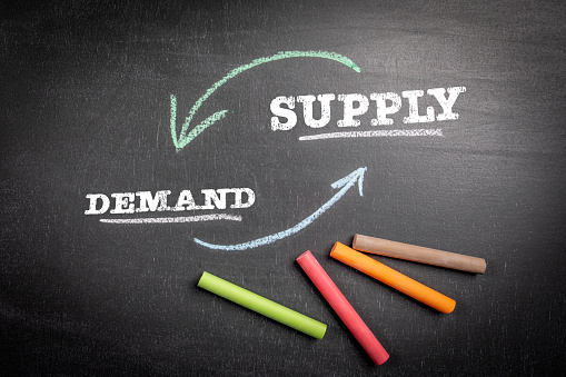 Demand and Supply Concept. Text and colored pieces of chalk on a dark board.