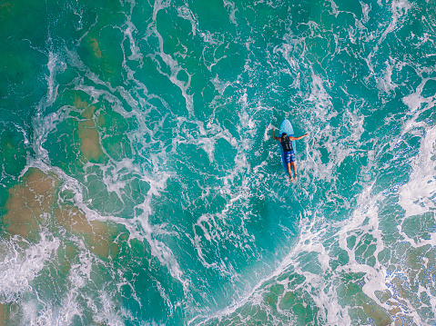 directly above asian chinese male surfer swimming toward wave