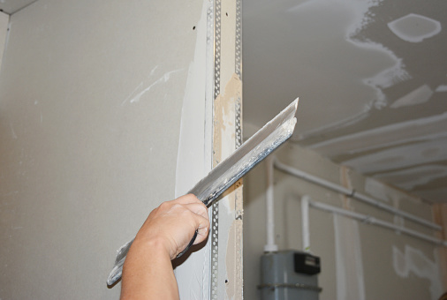 Builder plastering, skim coating, finishing, applying the first coat of plaster on a drywall partition wall  during house renovation.