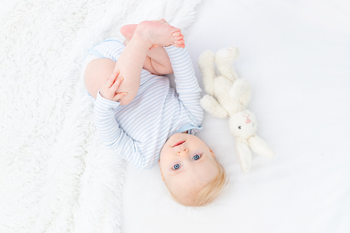 baby blonde boy six months old on bed with toy