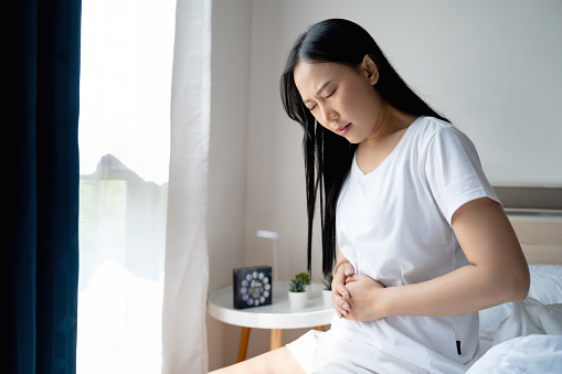 Asian woman unhappy suffers from stomach ache in the bedroom, She having stomachache because of menstruation or Chronic gastritis.