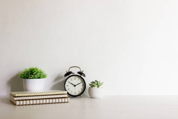 istock Minimal concept with notebooks, clock and cactus on wooden table with natural light. 1472469386