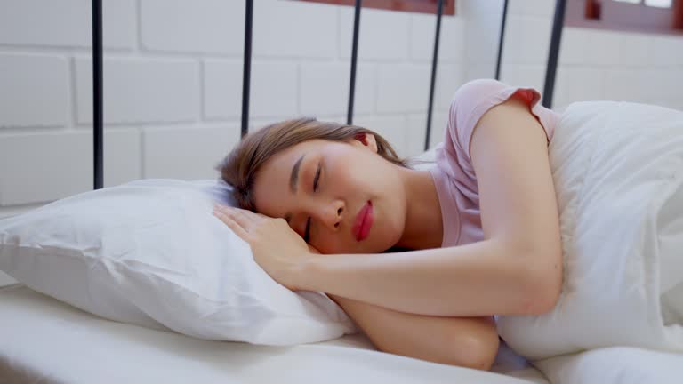 Asian beautiful woman sleeping with happiness in bedroom at home. Attractive young female in pajamas feeling happy and relax while lying down on bed with comfort blanket and pillow in morning in house