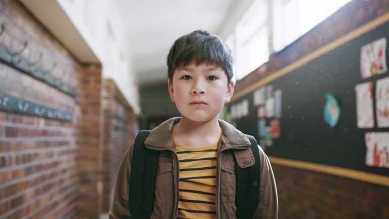 Serious child, portrait and face in school corridor for bullying awareness, children mental health or social anxiety. Sad Asian boy, kid and student in hallway with learning, education or studying