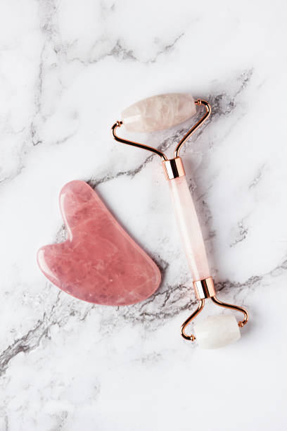 istock Pink jade roller and gua sha stone massager for face on white marble. 1472473156