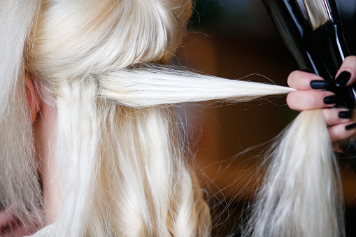Taking blonde customer's hair strands and using iron for curls, small business hairdresser's