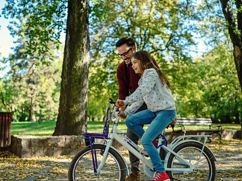 Father teaching his daughter to cycle in the park