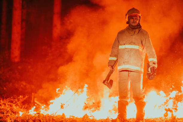 istock Firefighter at job. Firefighter in dangerous forest areas surrounded by strong fire. Concept of the work of the fire service 1472476483